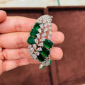 bracelet with green gemstones and silver accents held in a hand against a brown background