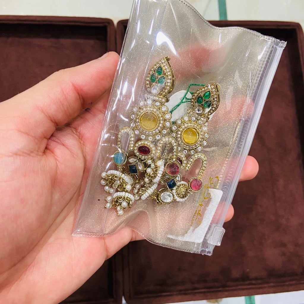 Hand holding a decorative brooch with gemstones in clear packaging.