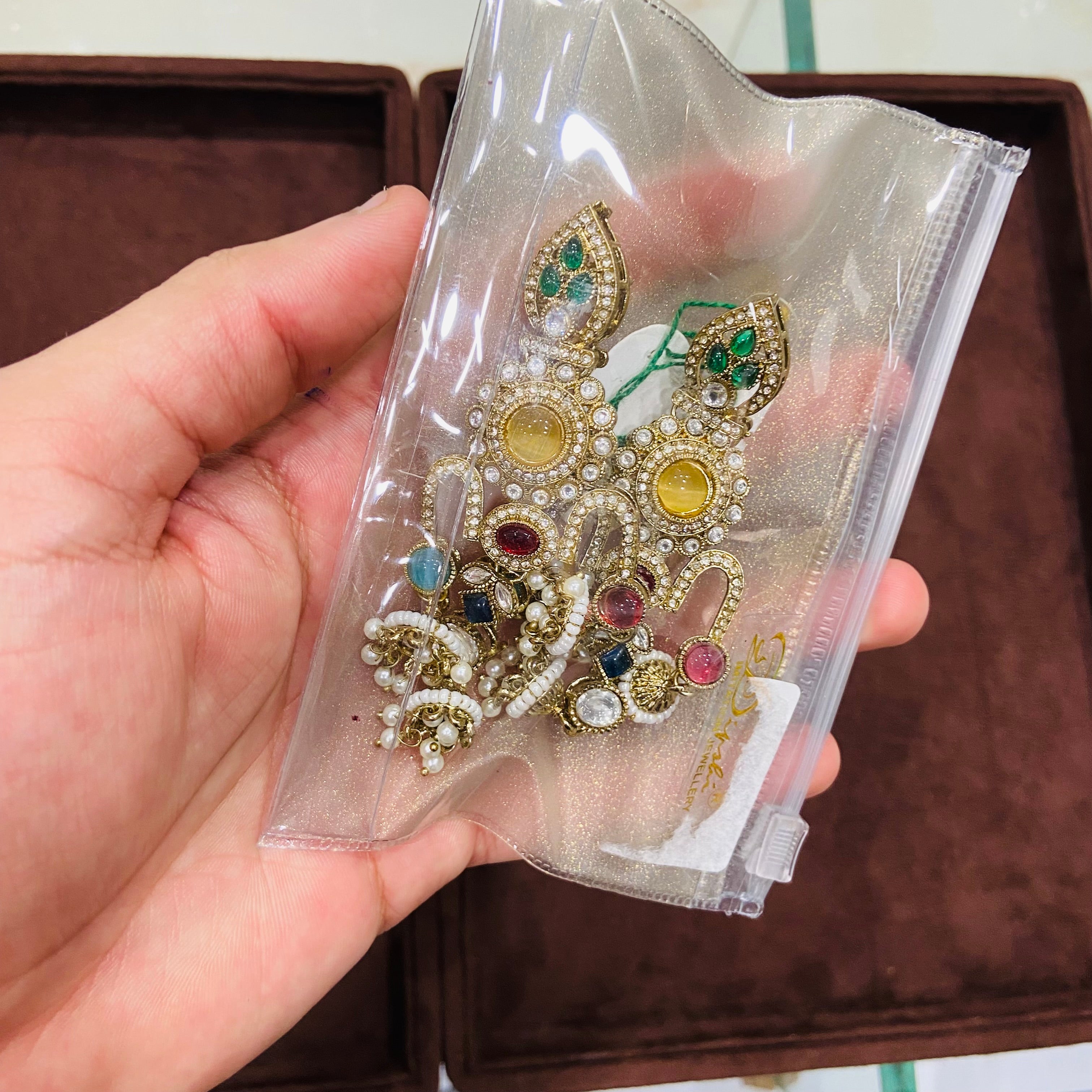 Hand holding a decorative brooch with gemstones in clear packaging.