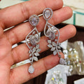 Diamond earrings held in a hand with a blurred jewelry box in the background