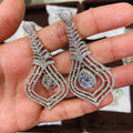 Delicate silver earrings with gemstones held in a hand against a blurred background