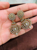 Ornate gold and diamond earrings held in a hand against a brown background