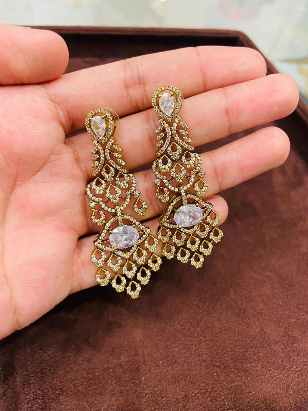 Gold earrings with gemstones held in a hand on a brown surface