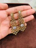 Gold earrings with gemstones held in a hand on a brown surface