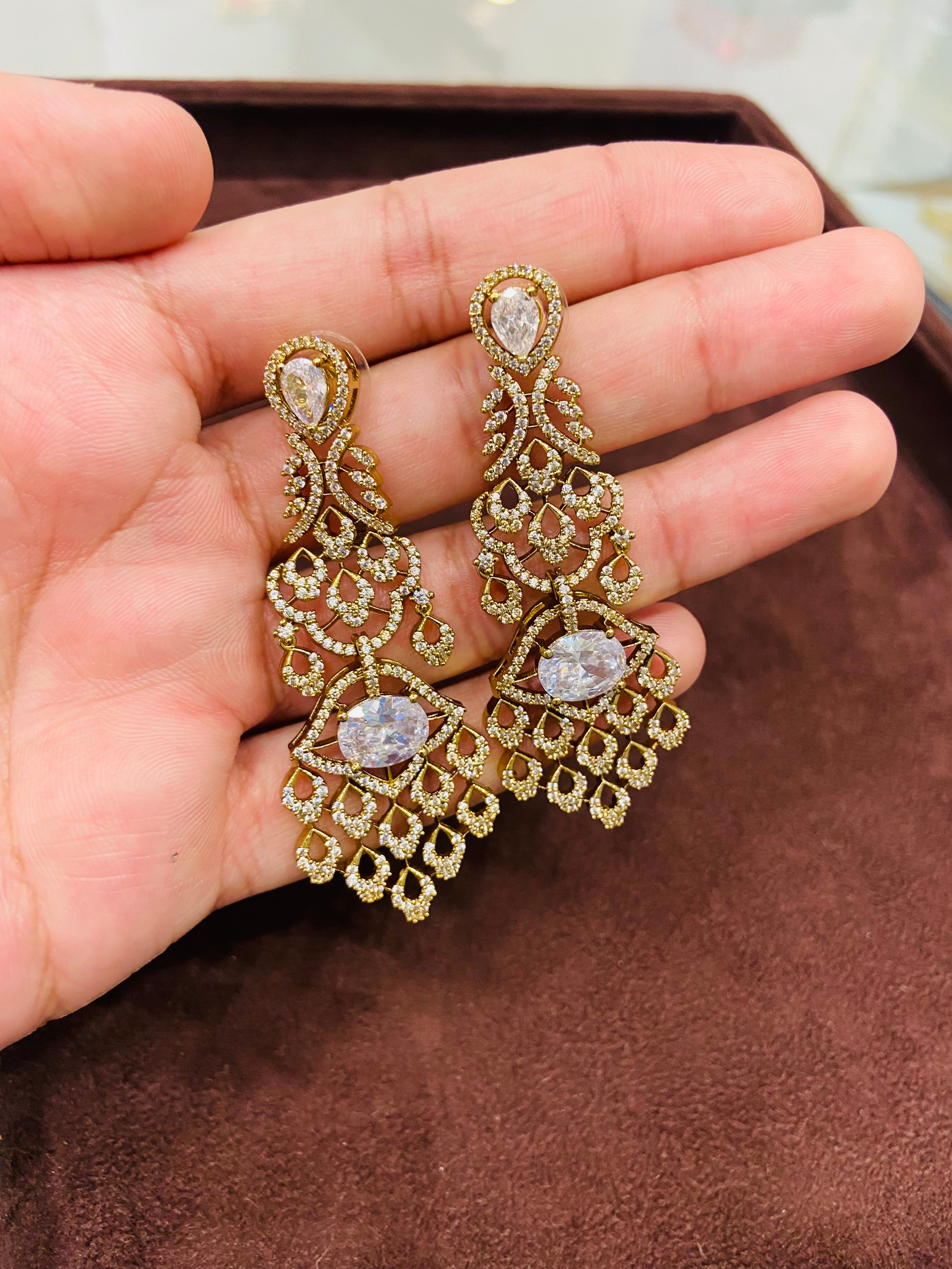 Gold earrings with gemstones held in a hand on a brown surface