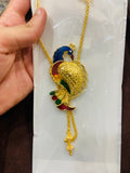 Gold peacock-shaped pendant on a chain held by a hand against a white background