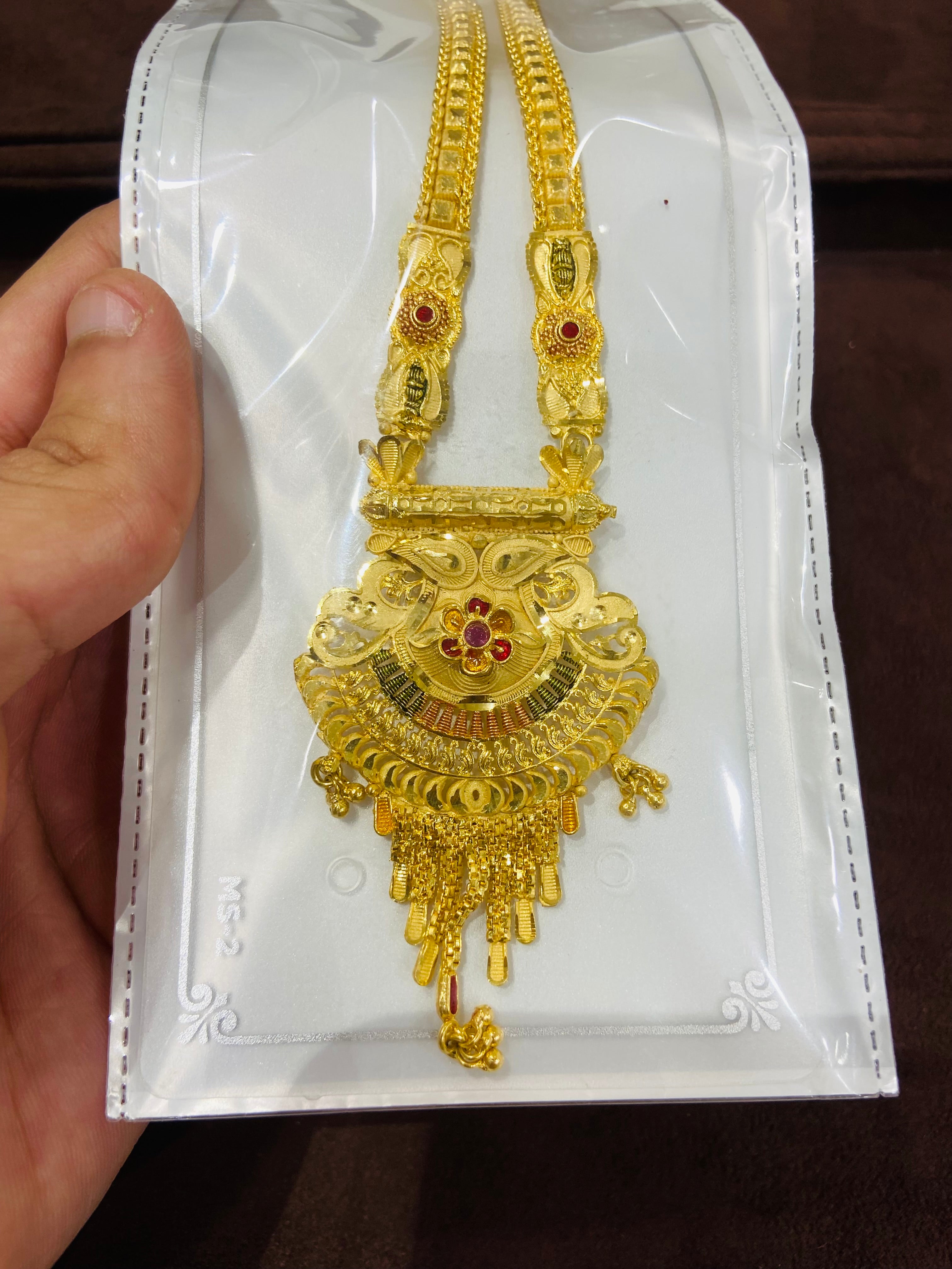 Gold necklace with pendant on a white card held by a hand.
