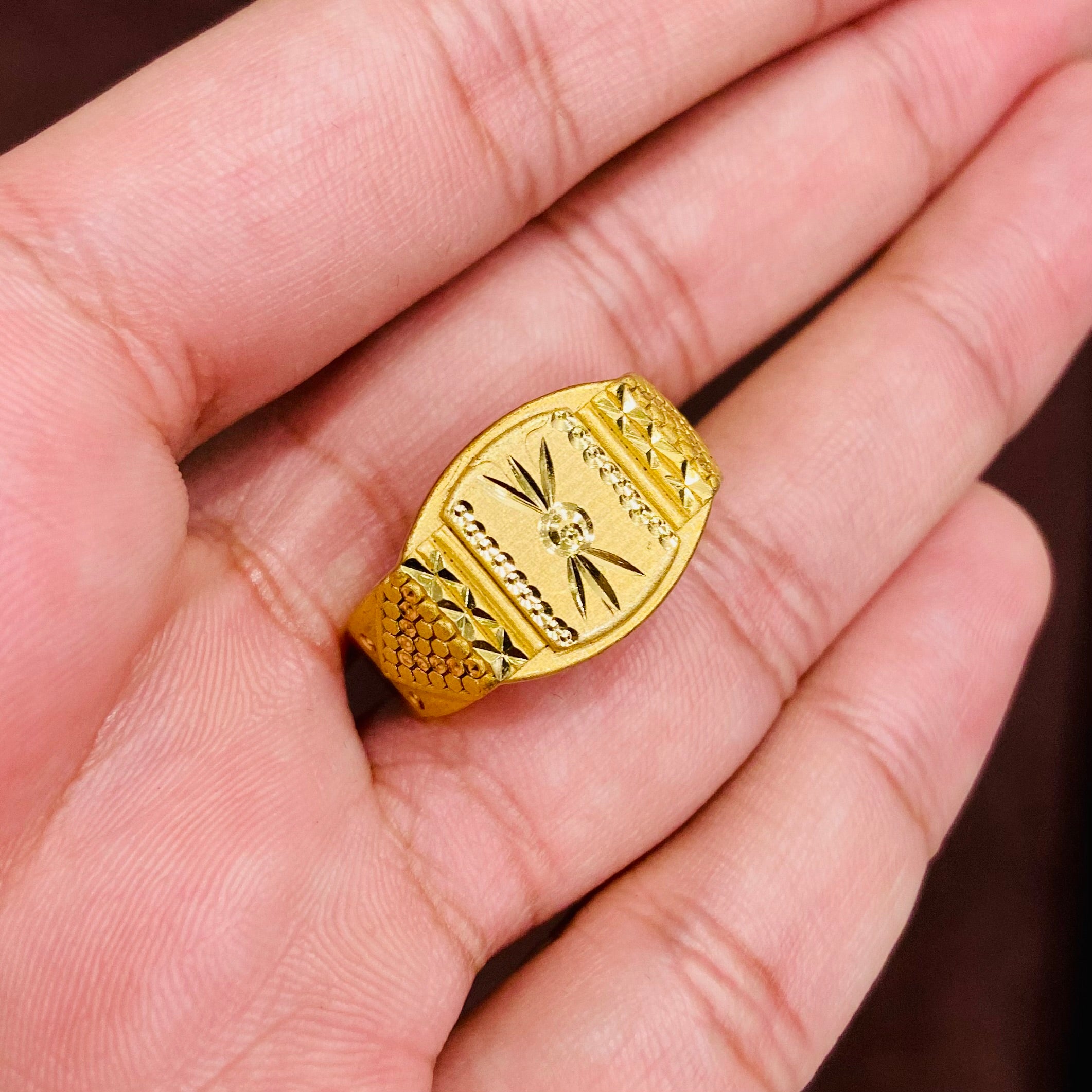 Gold ring with intricate design held in a hand against a neutral background
