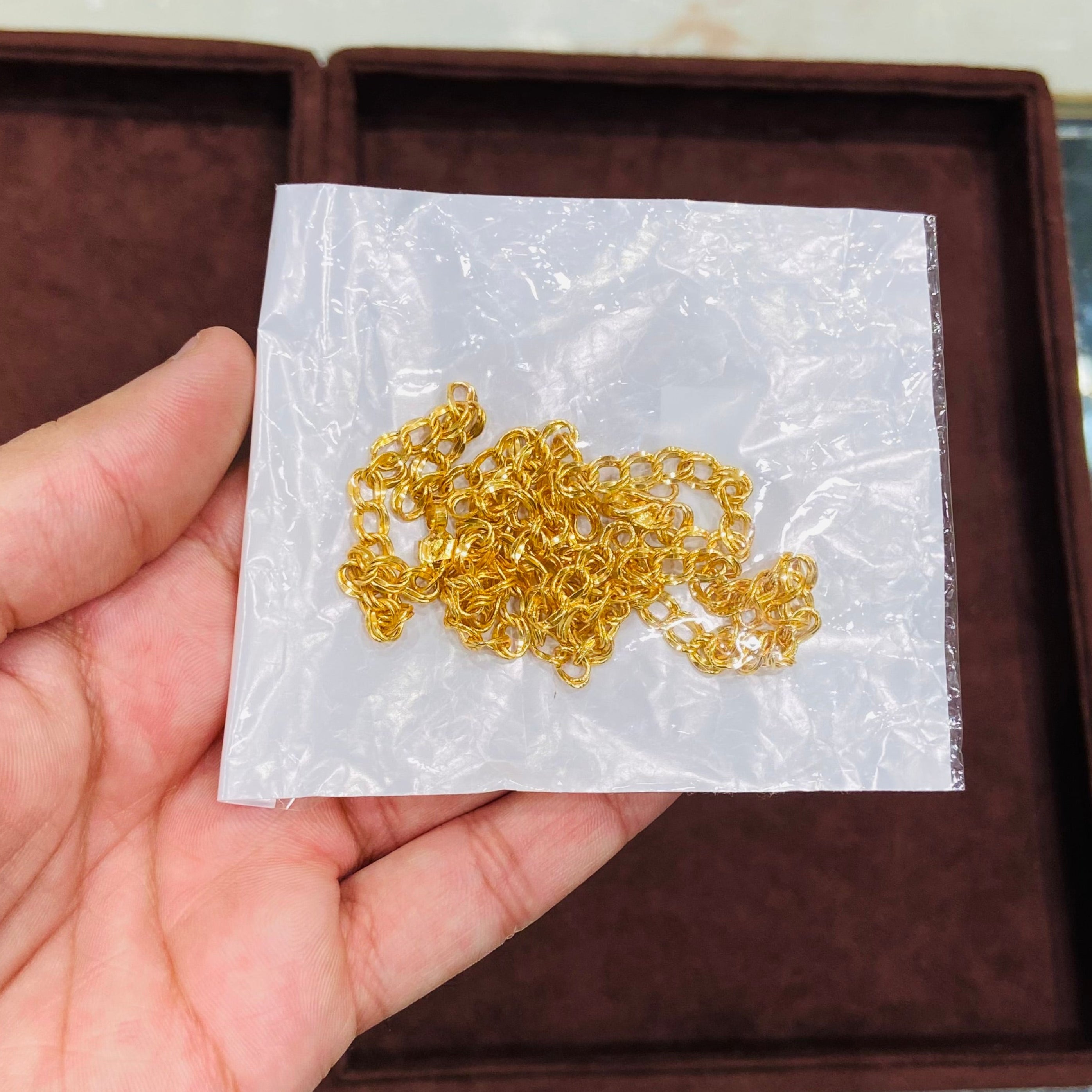 Gold chain on a white paper held by a hand, with a brown box in the background.