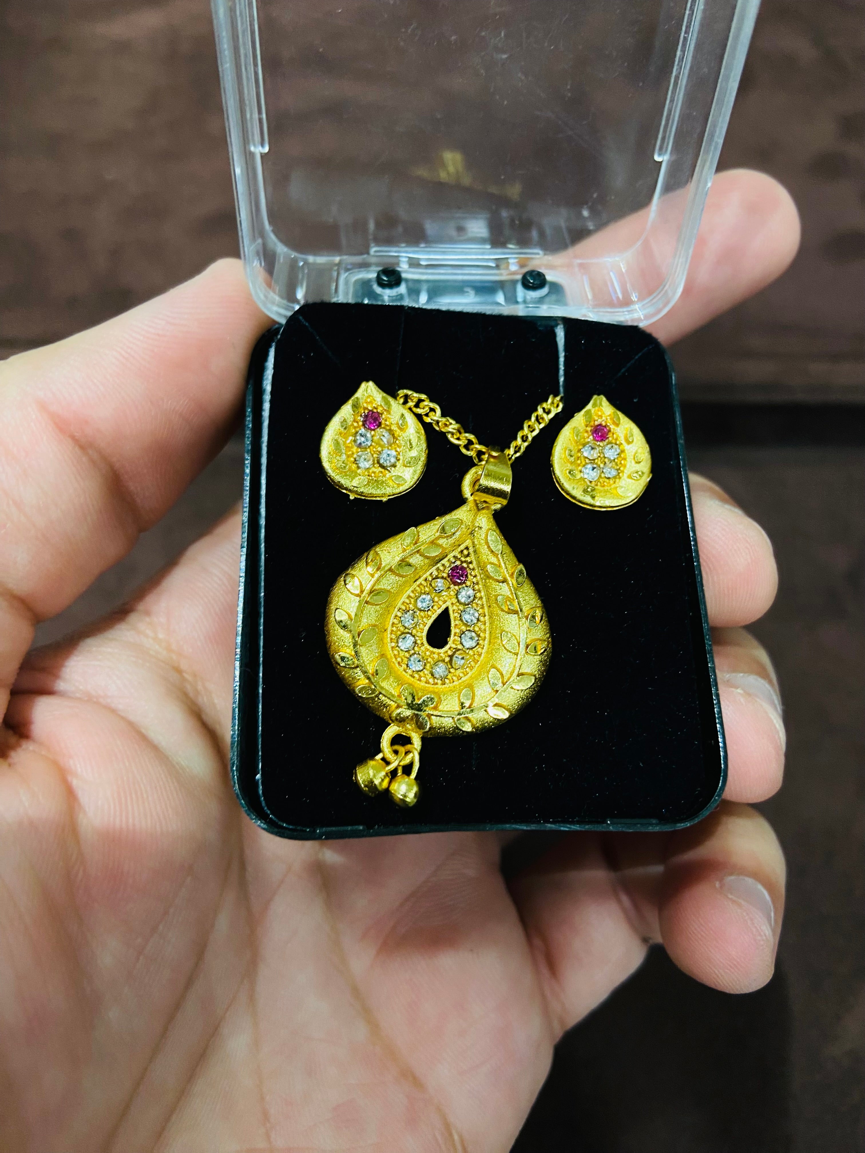 Gold jewelry set in a black box held by a hand