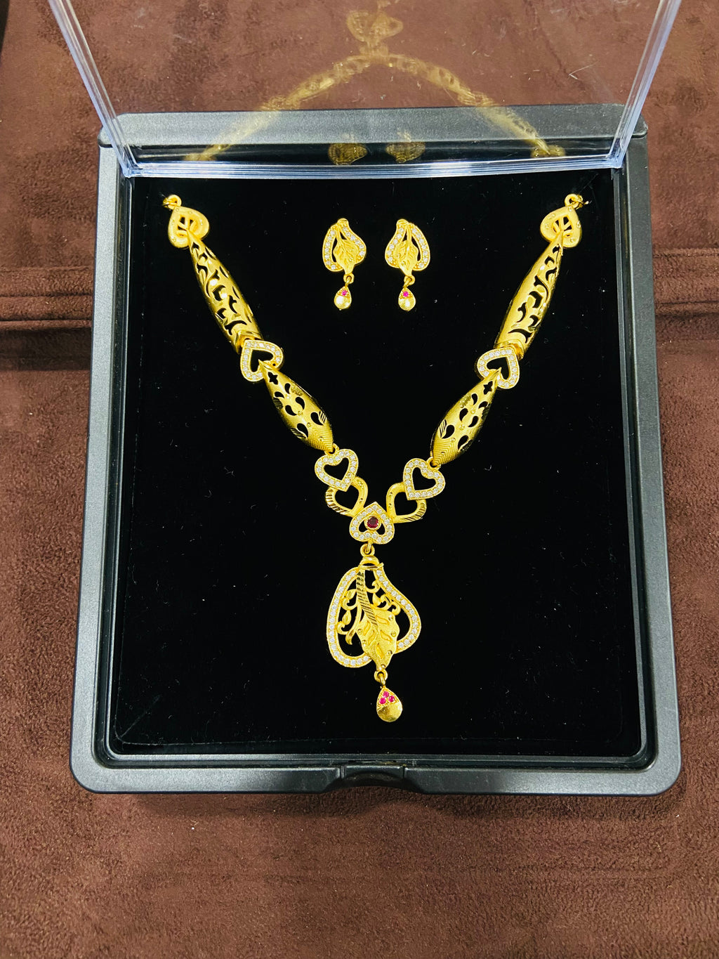 Gold necklace and earrings set in a clear display case on a brown surface.