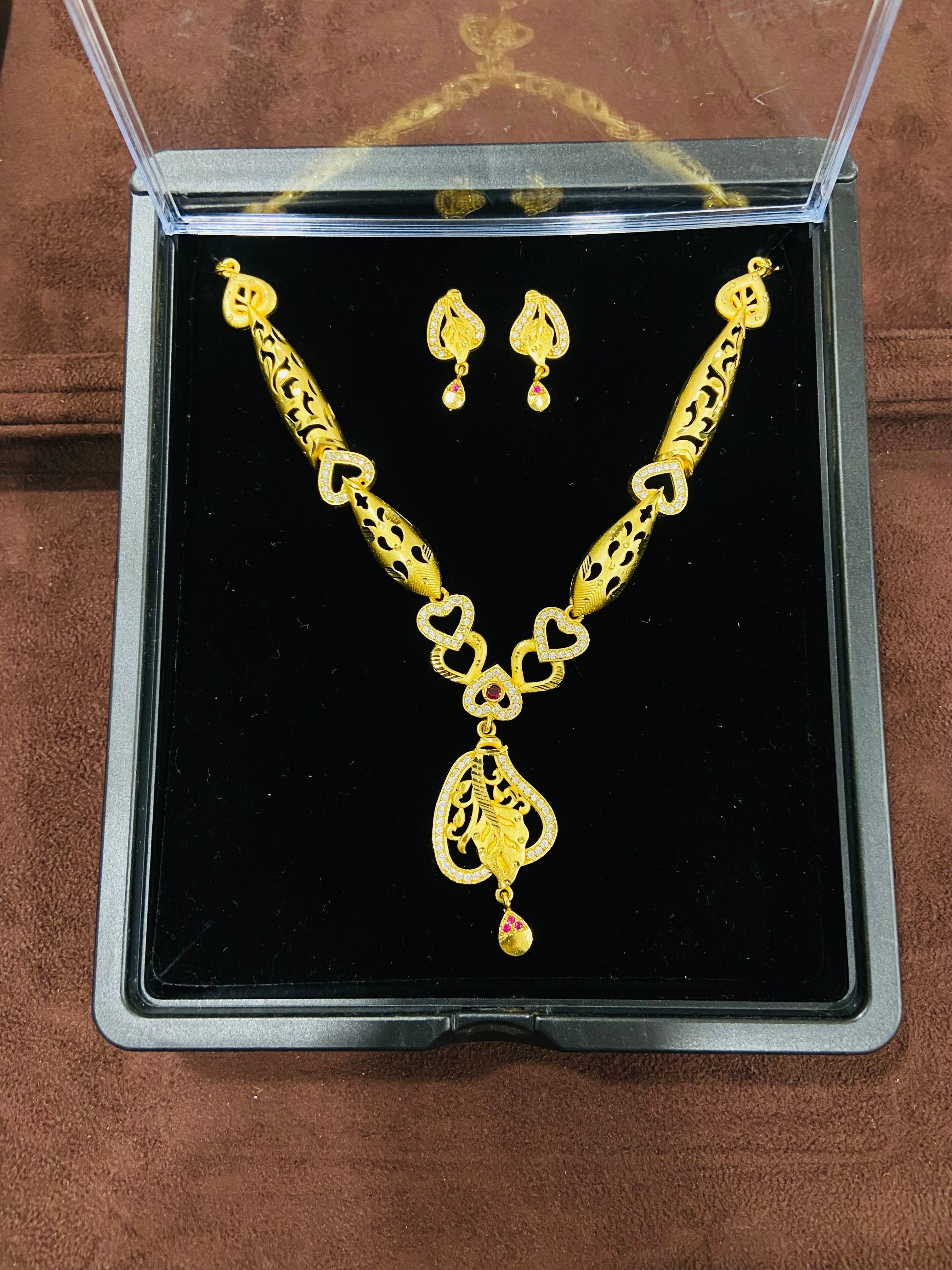 Gold necklace and earrings set in a clear display case on a brown surface.