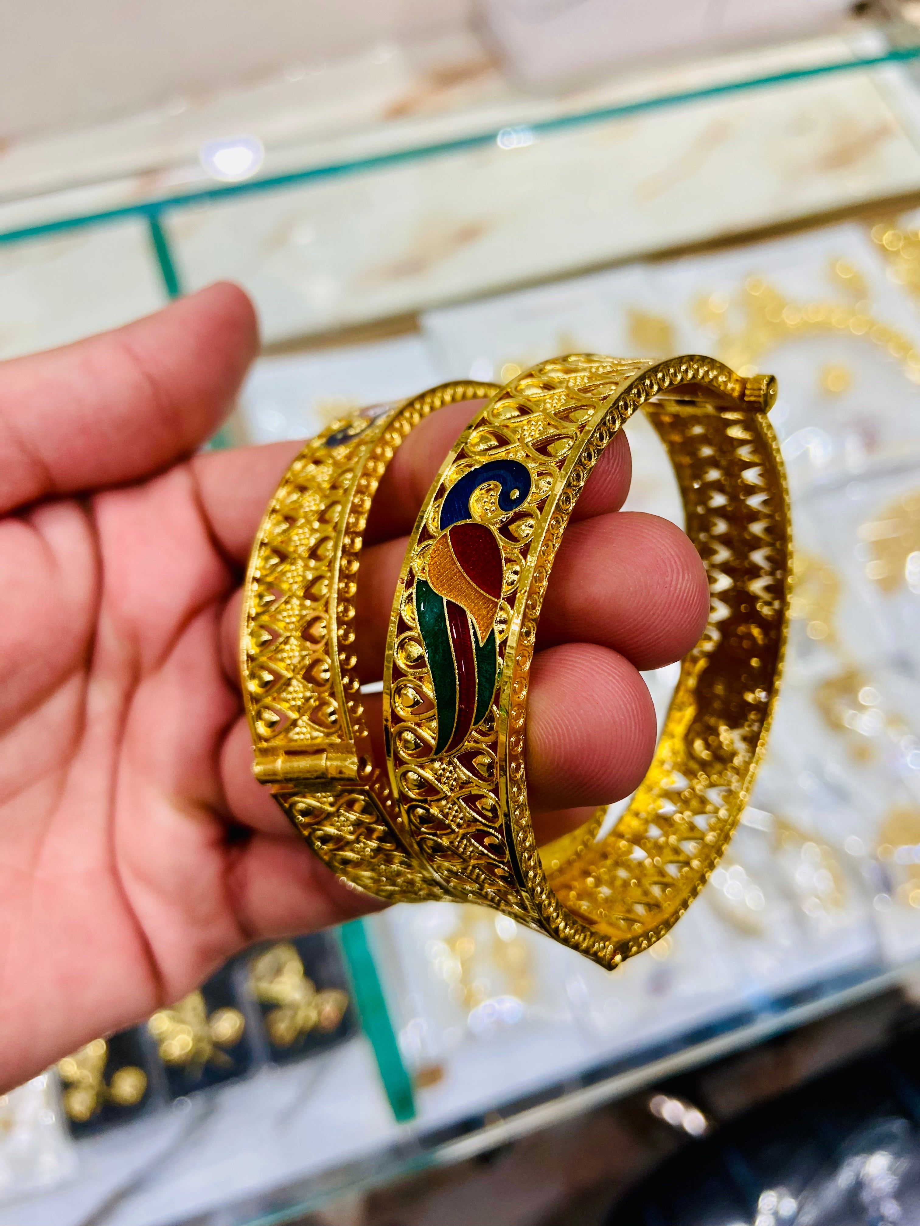 Gold bracelet with intricate design held by a hand on a reflective surface.