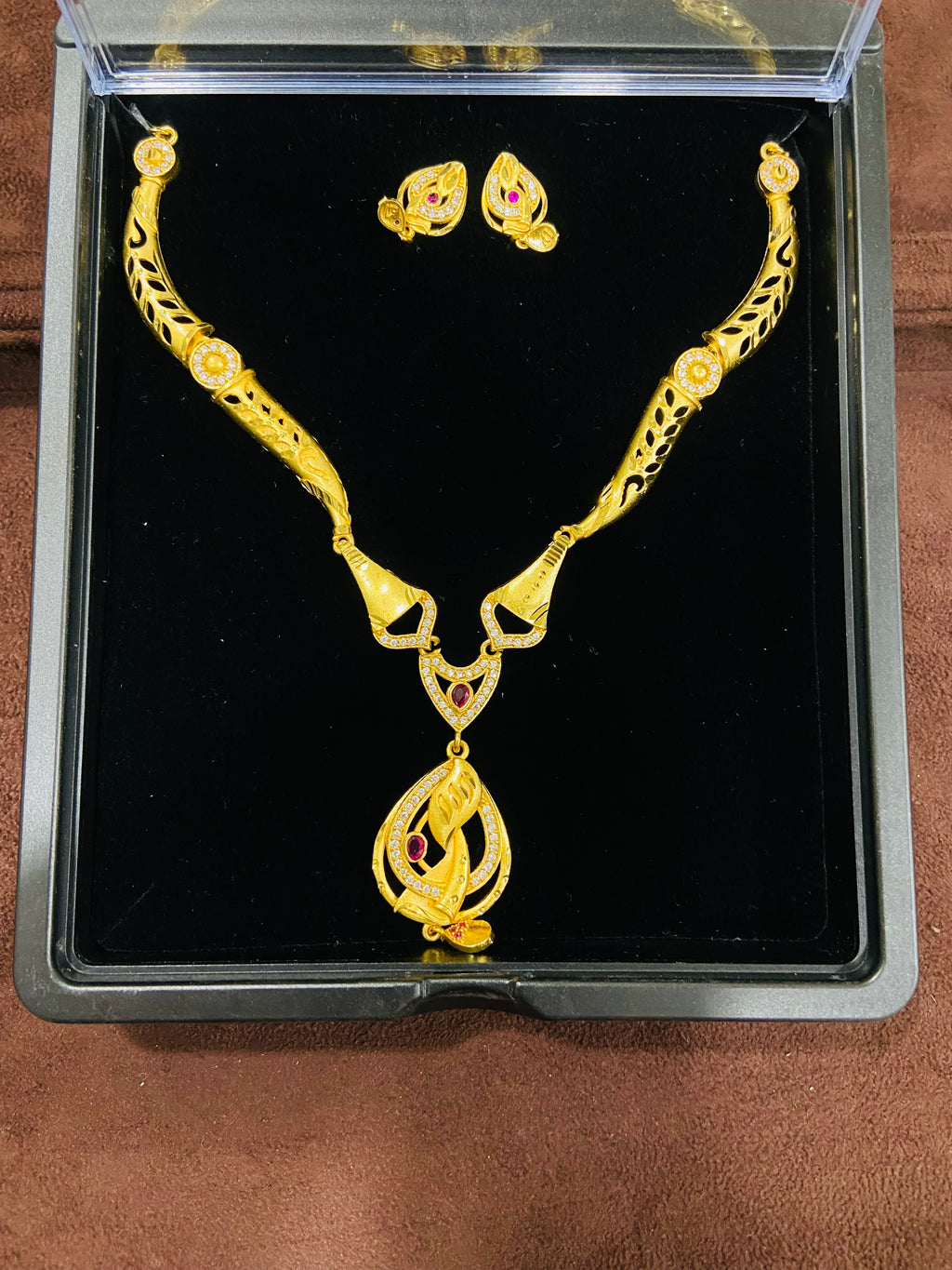 Gold necklace and earrings set in a black display box on a wooden surface