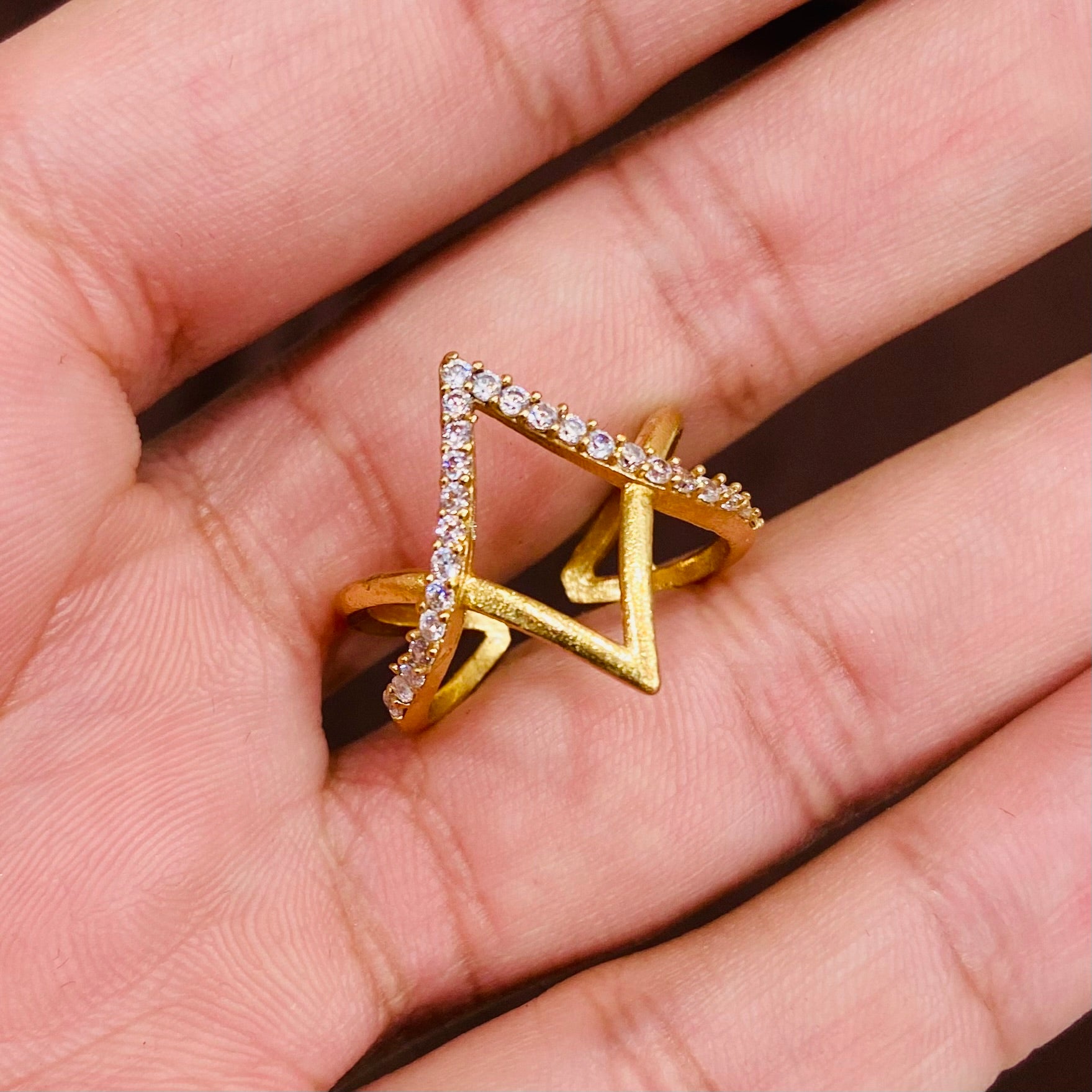 Gold triangle-shaped ring with embedded stones on a hand