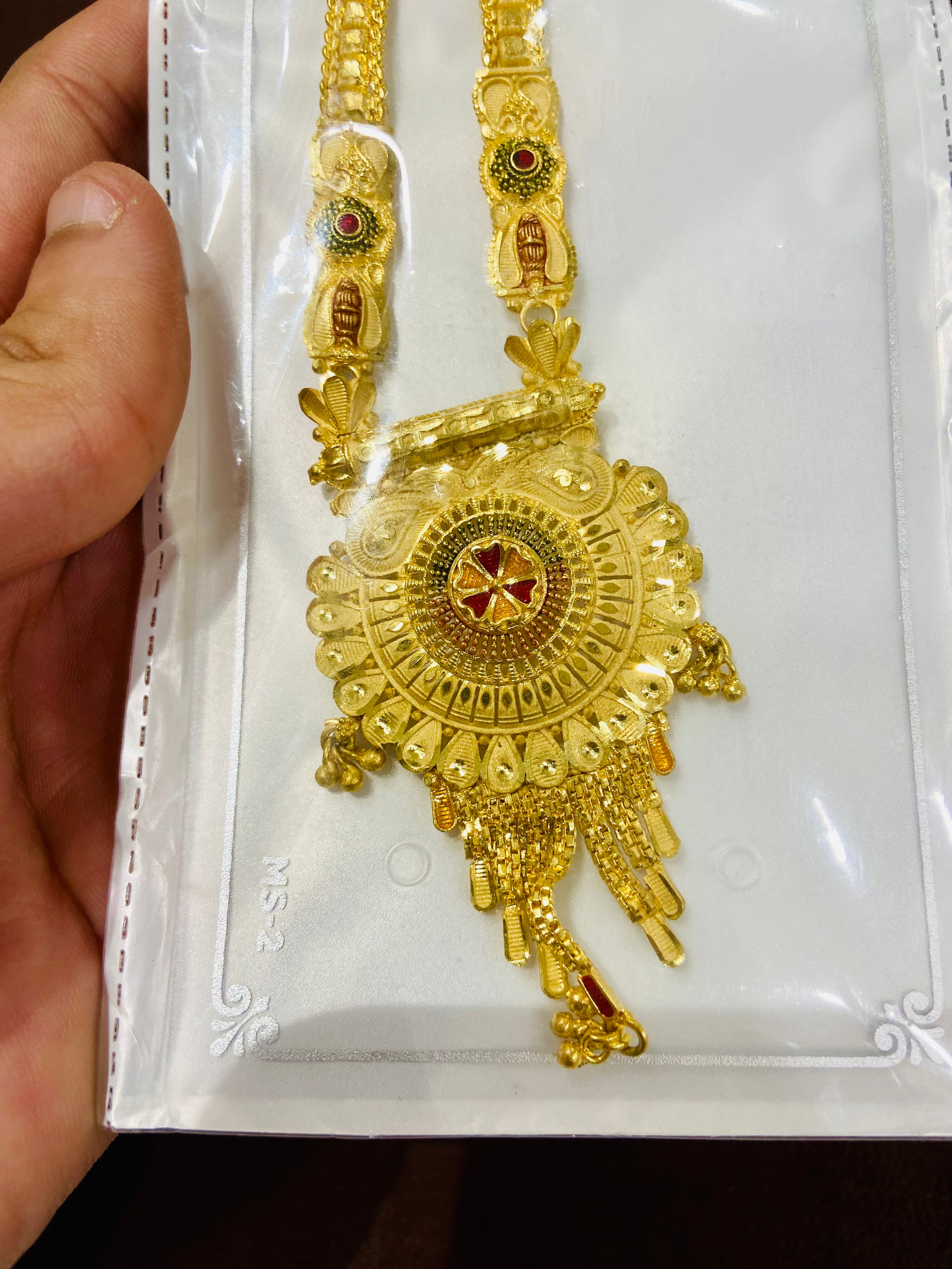 Gold necklace with intricate designs held by a hand on a white card.