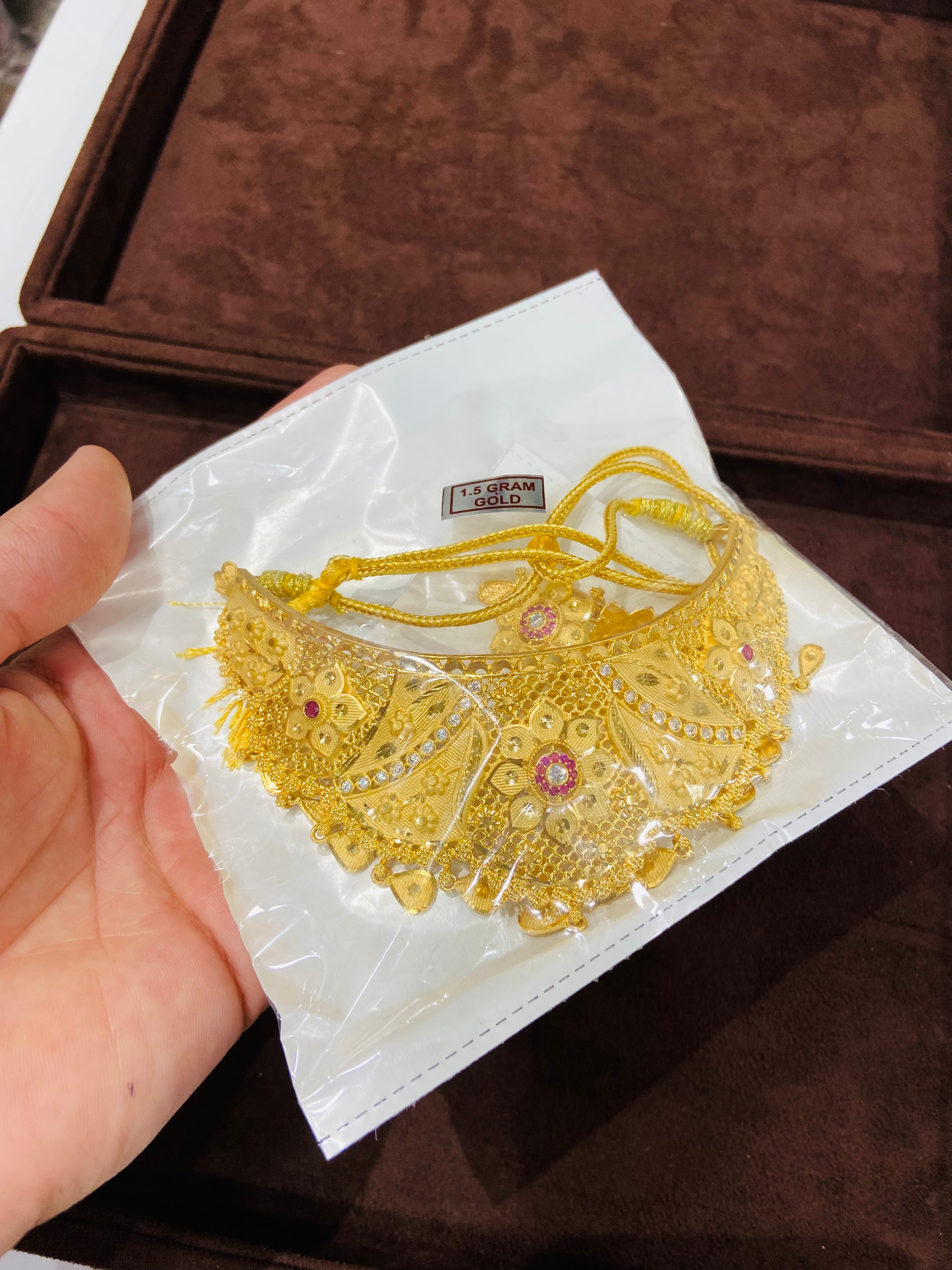 Gold necklace on a white paper with '18k Gold' label, held by a hand against a brown background.