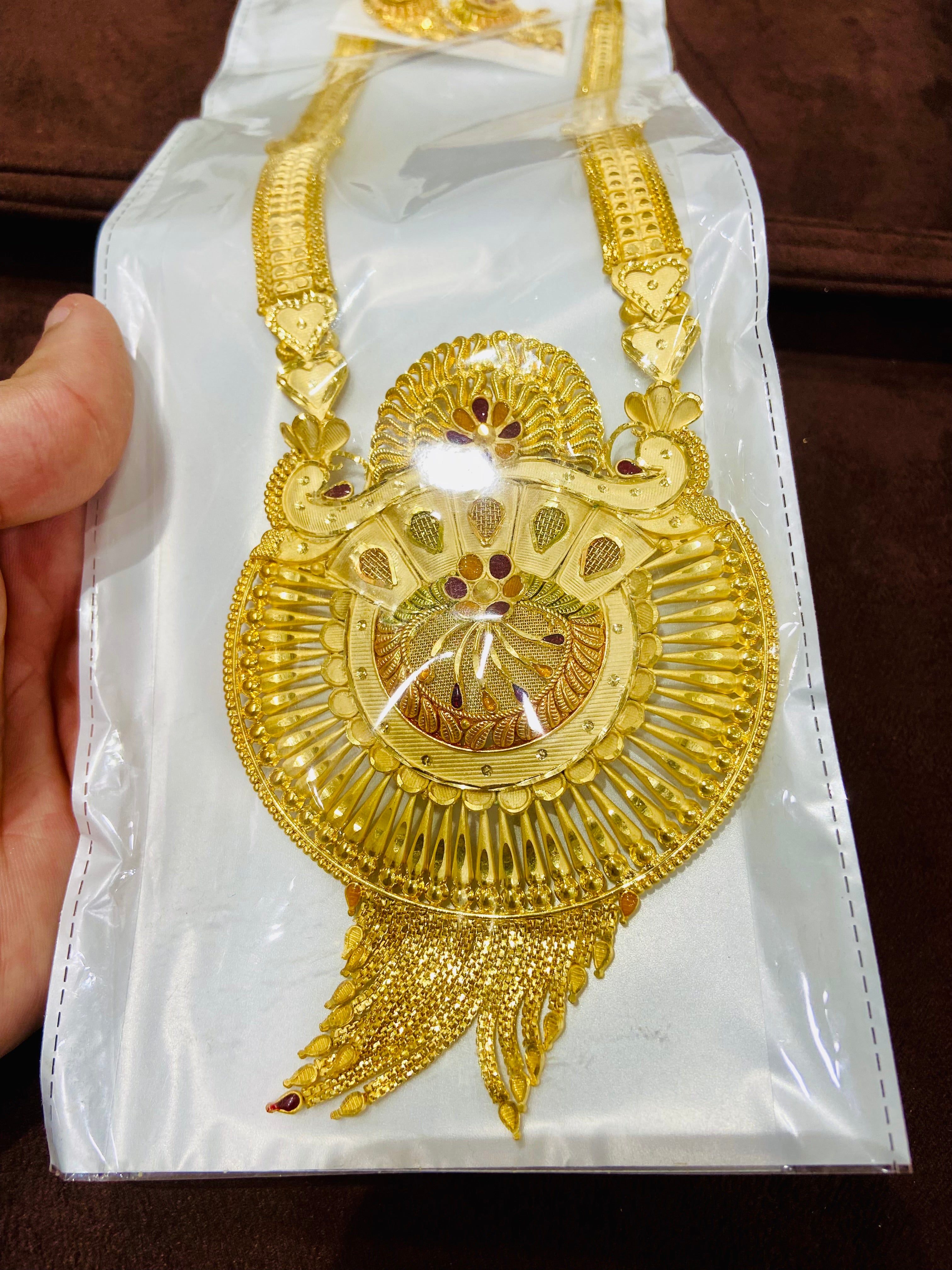 Gold necklace with intricate design on a white card, held by a hand.
