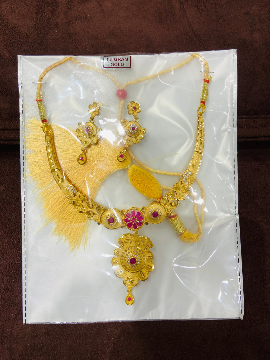 Gold necklace with pink gemstones on a white card with gold design