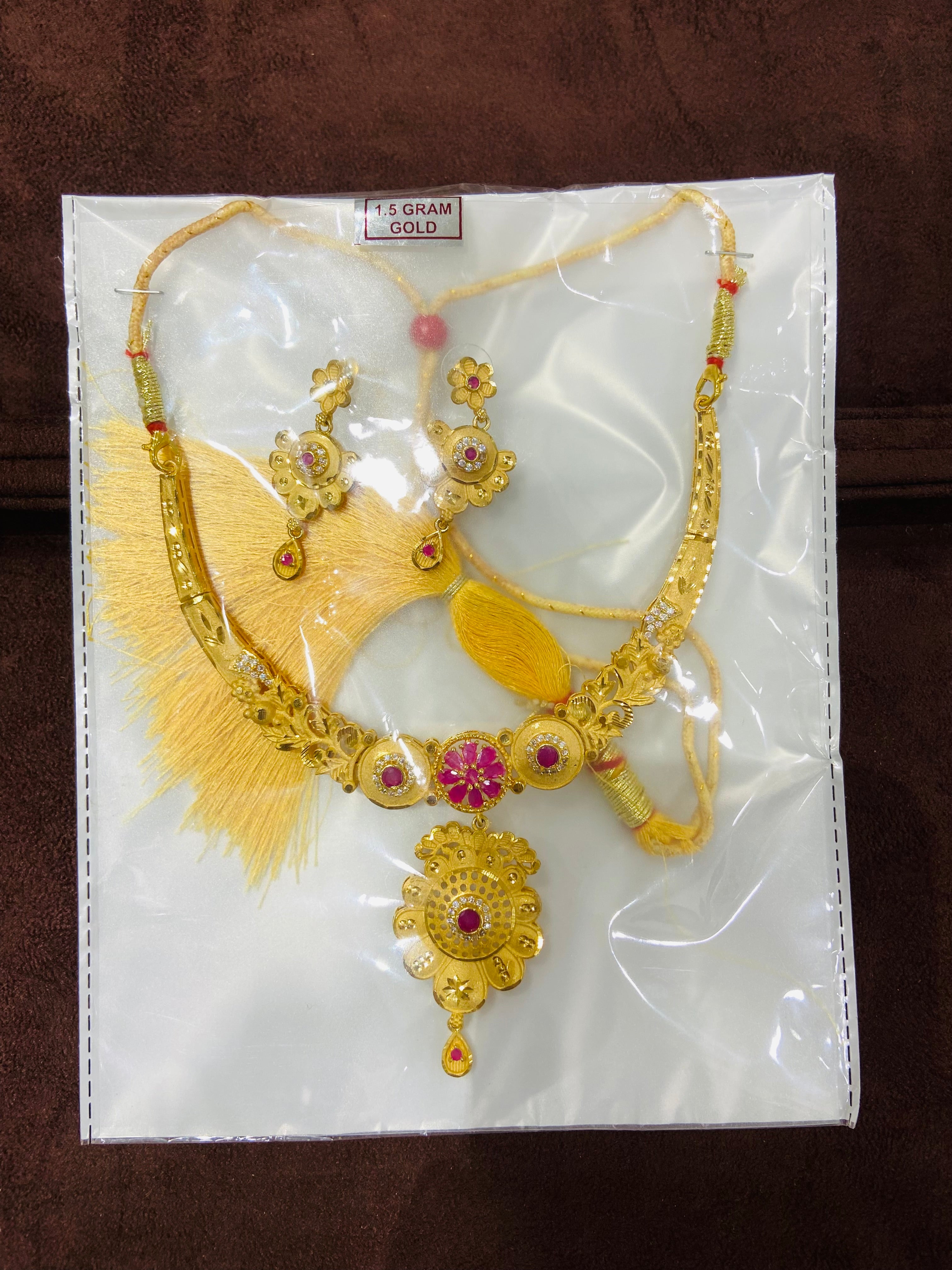 Gold necklace with pink gemstones on a white card with gold design